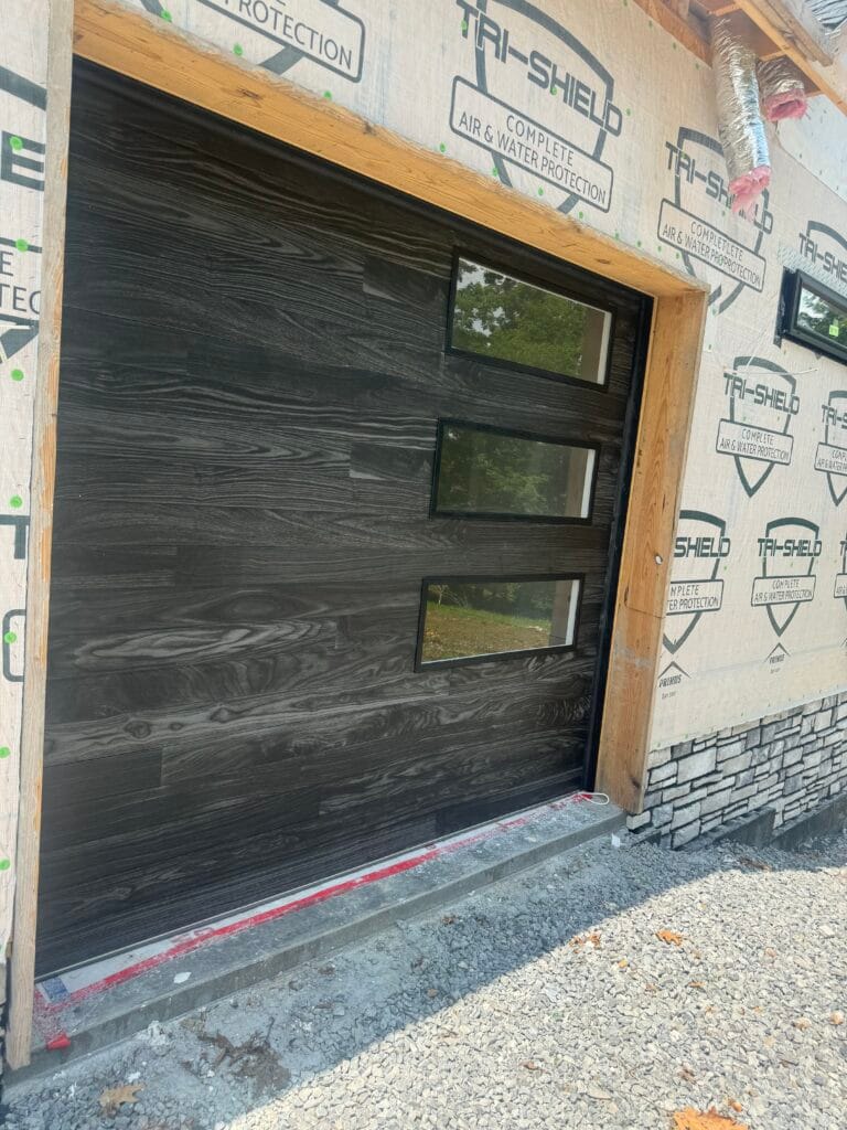 Dark wood-grain modern garage door with side windows on a new build