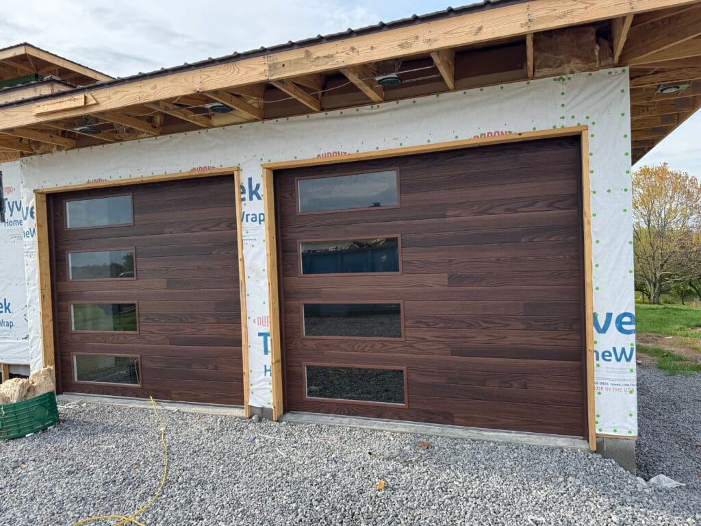 Two modern wood-grain garage doors with vertical windows on new construction in Kentucky