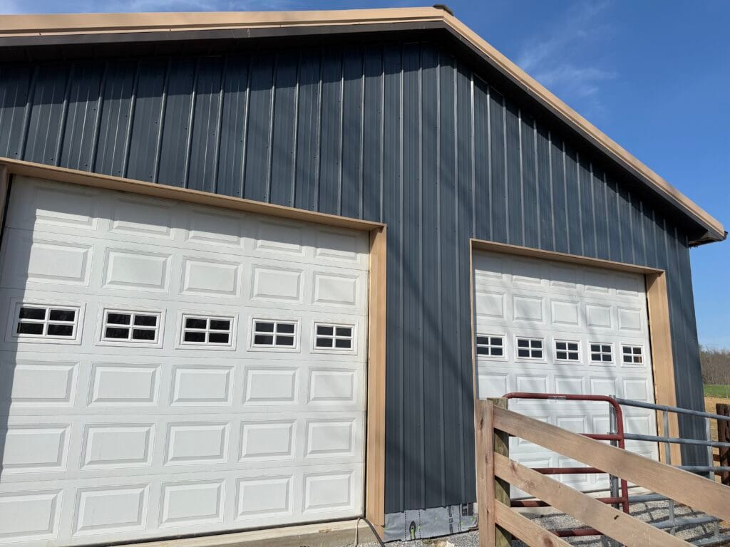 White raised-panel garage doors with windows on a dark steel pole barn in Central Kentucky